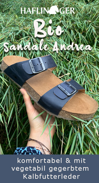 Hand h�lt Haflinger Bio Sandale vor Grashalmen