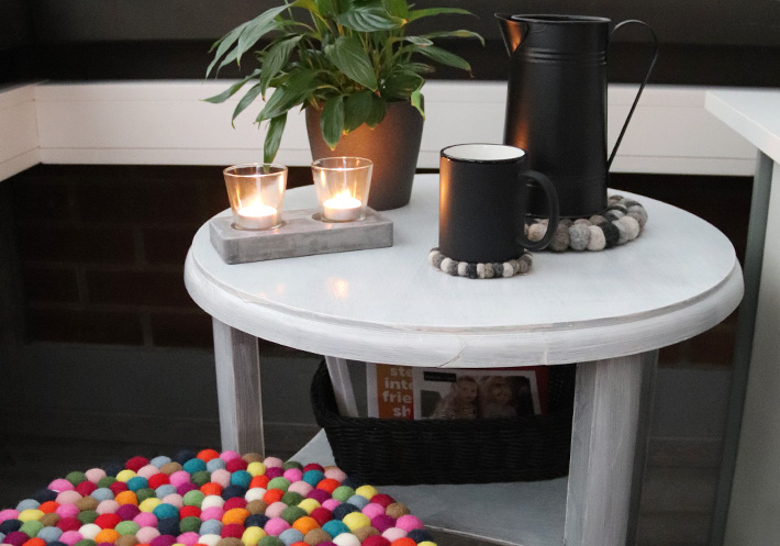 Schwarze Tasse und Kanne stehen auf Filz Untersetzern neben Pflanze und Teelicht