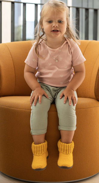 Kind sitzt auf einer Couch und l�sst F��e mit H�ttenschuhen baumeln.